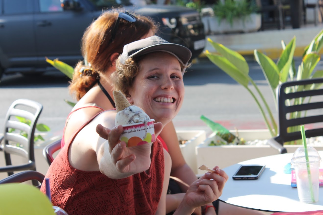 En una terraza, una persona sentada sonríe mientras muestra una tarrina de helado