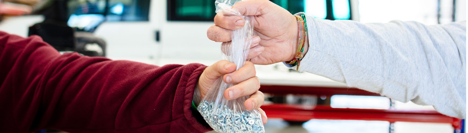 Manos de dos personas intercambiando una bolsa de tornillos en un almacén